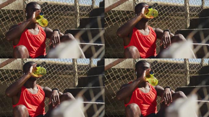 疲惫的非洲裔美国人坐着，喝着水瓶，在户外运动中休息