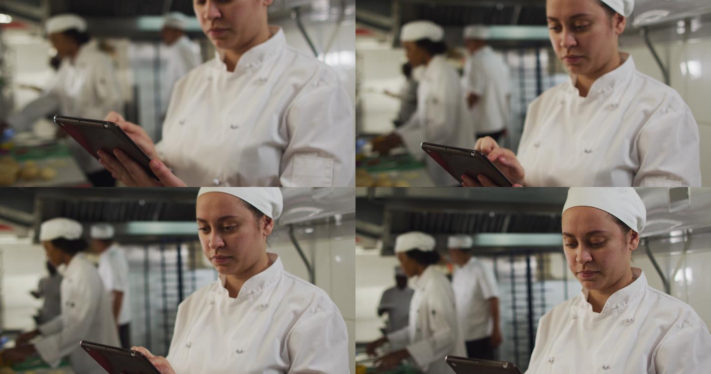 白人女厨师使用平板电脑在餐厅厨房与其他厨师的背景