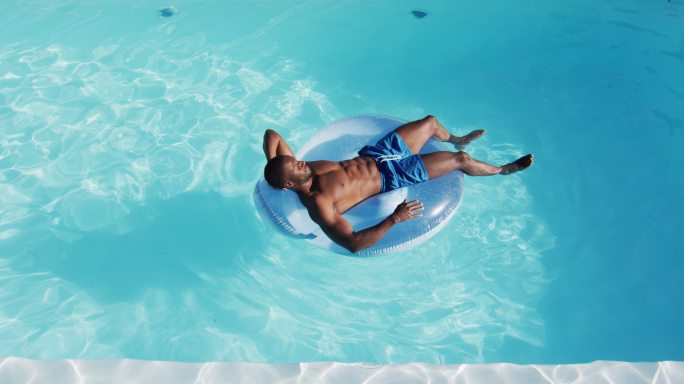 混合种族的人有乐趣日光浴在充气游泳池