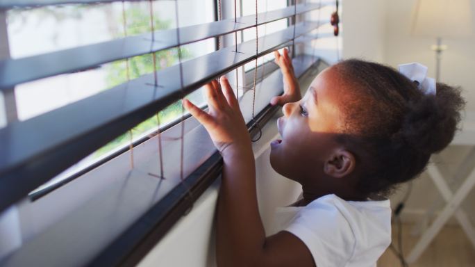 一个非裔美国女孩在家里看着窗外