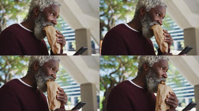 非裔美国老人在企业园区吃零食用智能手机