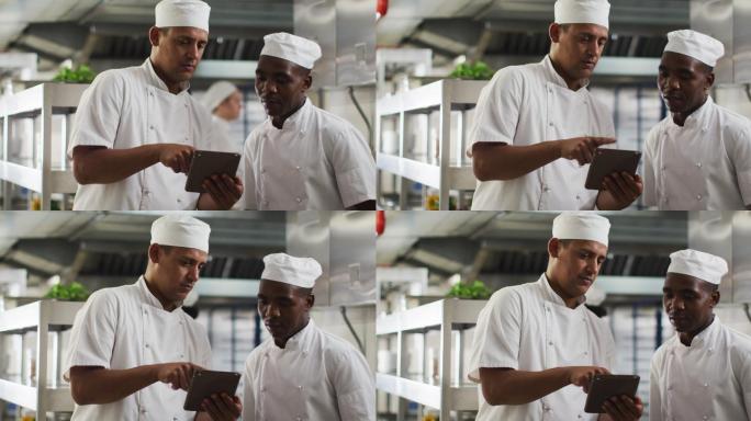 两个不同的男厨师在餐厅厨房里聊天和使用平板电脑