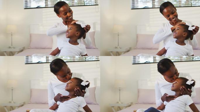 快乐的非裔美国母女坐在床上，母亲把头发扎成蝴蝶结