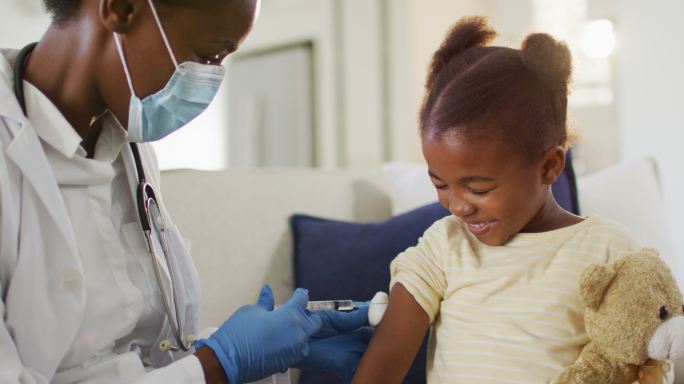 非裔美国女医生戴着口罩给家里微笑的女孩注射疫苗