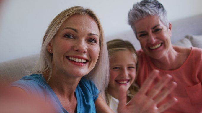 白人奶奶、母亲和女儿在家里用智能手机视频通话时挥手致意