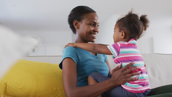 快乐的非裔美国母亲和女儿坐在沙发上，抚摸着额头
