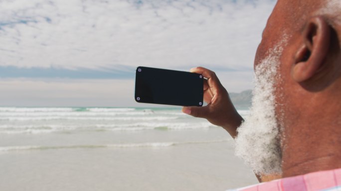 一名混血儿老年男子在海滩上用智能手机自拍