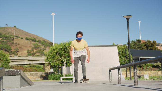 一名白人男子戴着口罩，在阳光明媚的日子里骑滑板、跳滑板