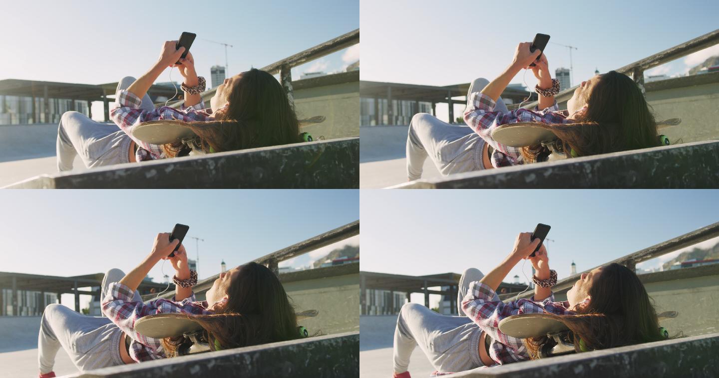 白种女人，撒谎，在一个阳光明媚的日子在滑板场用智能手机