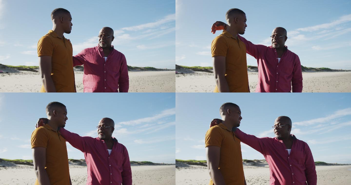 一位非裔美国父亲站在沙滩上，手搭在十几岁儿子的肩膀上说话