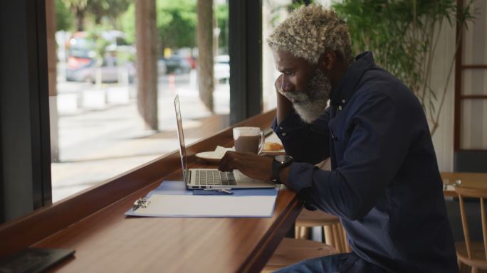 一位非裔美国老人坐在咖啡馆里使用笔记本电脑