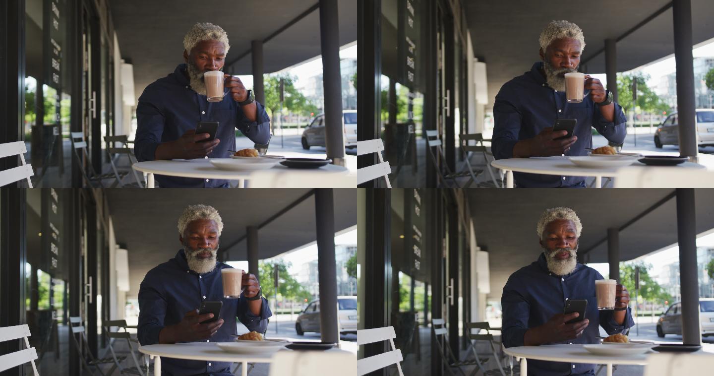 一位非裔美国老人坐在户外的咖啡馆边喝咖啡边用智能手机