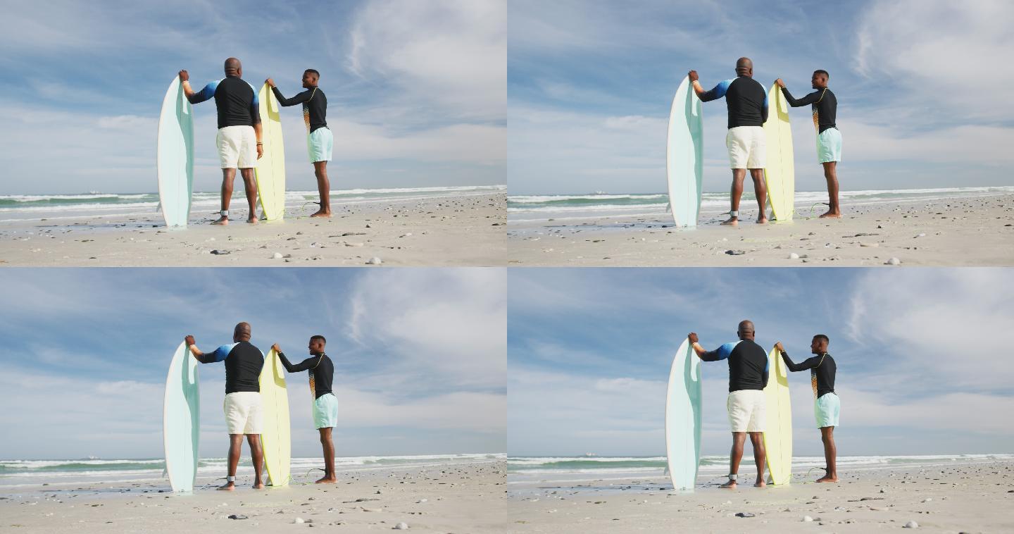 非裔美国父亲和十几岁的儿子站在海滩上，手里拿着冲浪板聊天