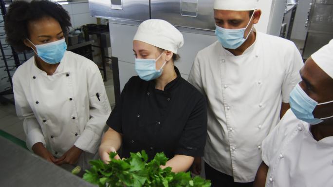 各式各样的厨师戴着口罩在餐厅厨房里看着蔬菜