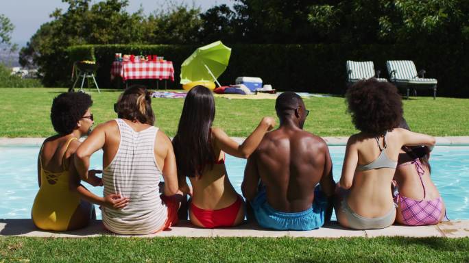 一群不同的朋友在泳池聚会上坐在一排