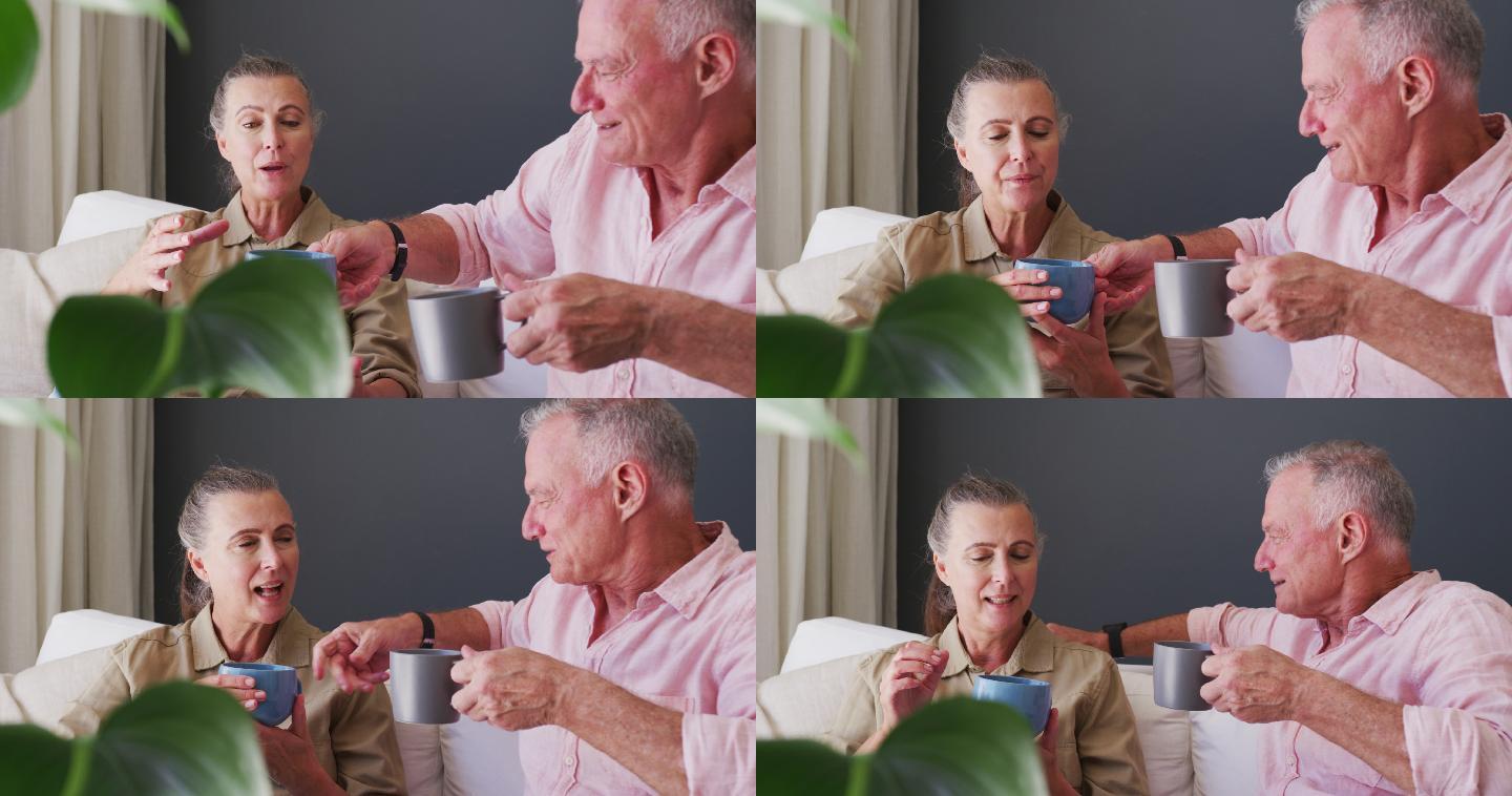 一对白人老年夫妇拿着咖啡杯坐在家里的沙发上聊天