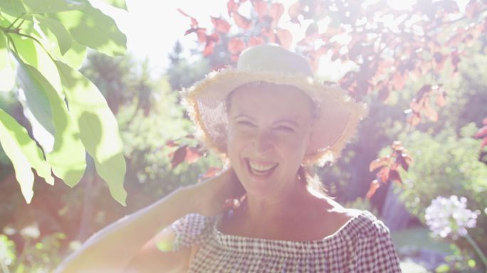 幸福的白人老年妇女的肖像在花园里戴着太阳帽和在阳光下微笑