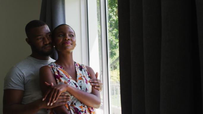 一对非洲裔美国夫妇在家里看着窗外，互相拥抱