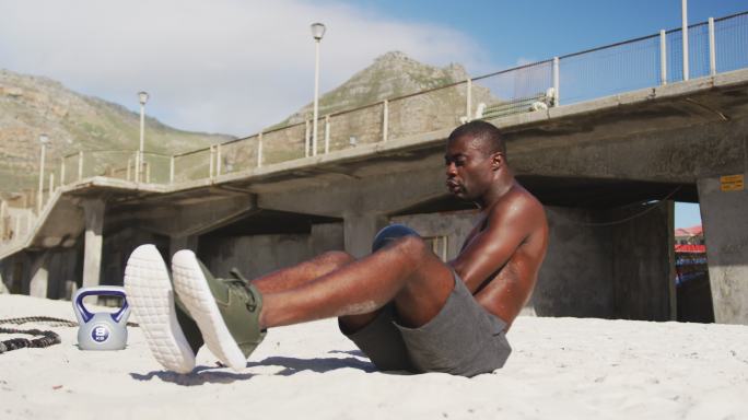 专注的非洲裔美国人做扭转球，在户外海滩锻炼