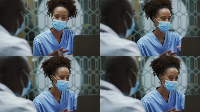 不同的男、女医生戴着口罩，讨论在办公室使用笔记本电脑