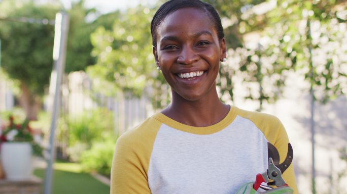 非裔美国妇女的肖像，拿着剪报看着相机和微笑在花园里