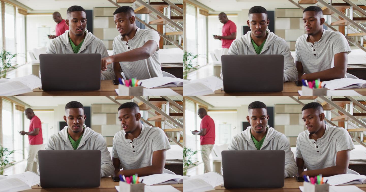 一对非洲裔美国青少年双胞胎兄弟一边用笔记本电脑一边和父亲聊天