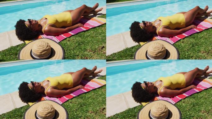 混血妇女躺在毯子上，在泳池边晒太阳