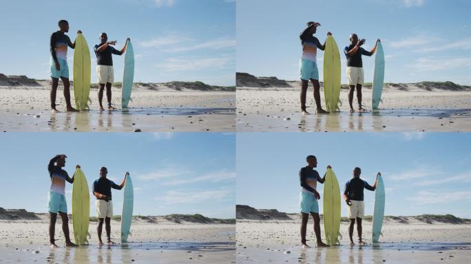 一对非裔美国父亲和十几岁的儿子站在海滩上，手里拿着冲浪板聊天