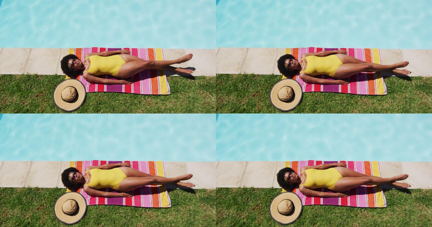 混血妇女躺在毯子上，在泳池边晒太阳