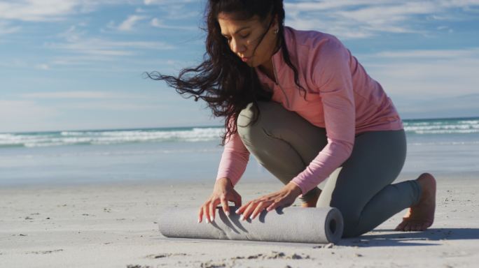 混血儿妇女在沙滩上滚动瑜伽垫