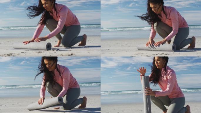 混血儿妇女在沙滩上滚动瑜伽垫