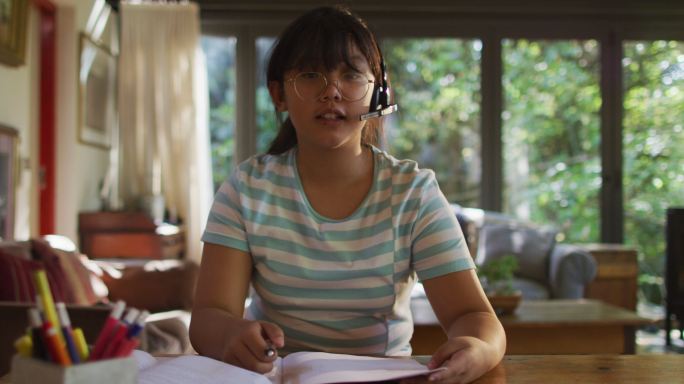 亚洲女孩坐在餐桌上戴着耳机和视频通话