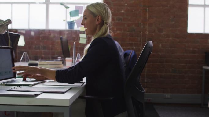 一位白人女商人坐在办公桌旁，用电脑向女同事传递文件