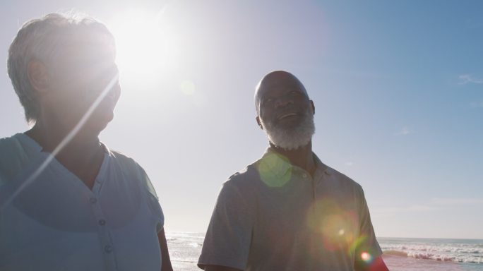 微笑的老非洲裔美国夫妇在海滩上手牵着手散步