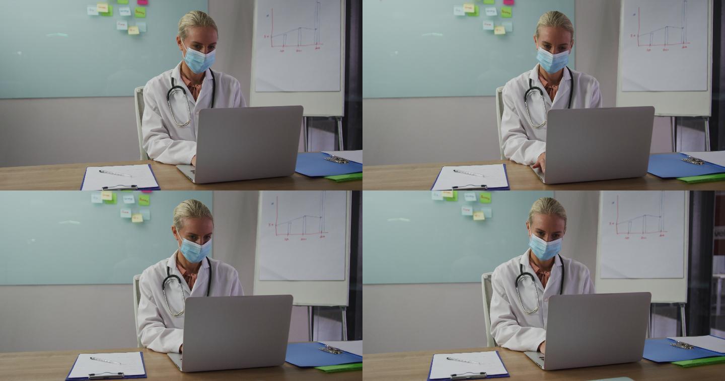白种女医生戴着口罩，坐在会议室的桌子上用笔记本电脑