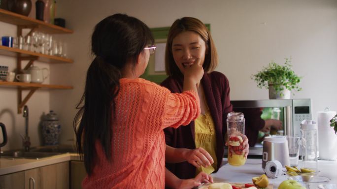 亚洲母亲和女儿在厨房准备健康饮料微笑