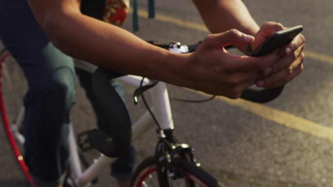 非洲裔美国人在城市，坐在自行车在街道上使用智能手机