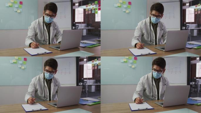 亚洲男医生戴着口罩坐在会议室的桌子前做笔记
