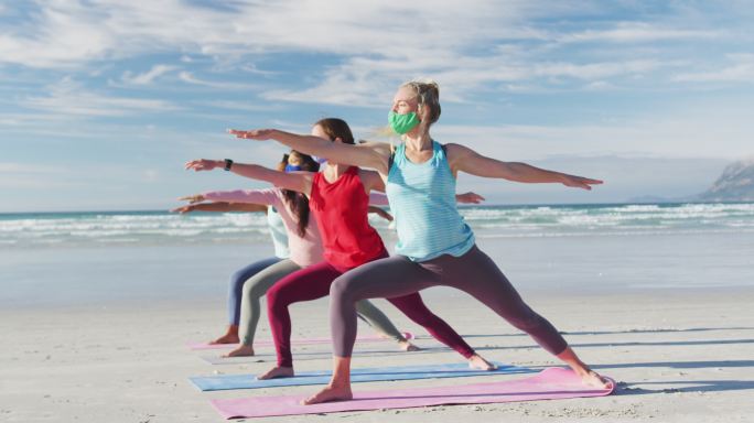一群不同类型的女性朋友戴着口罩在海滩上练习瑜伽