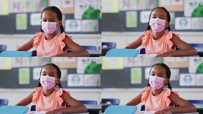 混血儿女学生的肖像戴着口罩，坐在教室里看着相机
