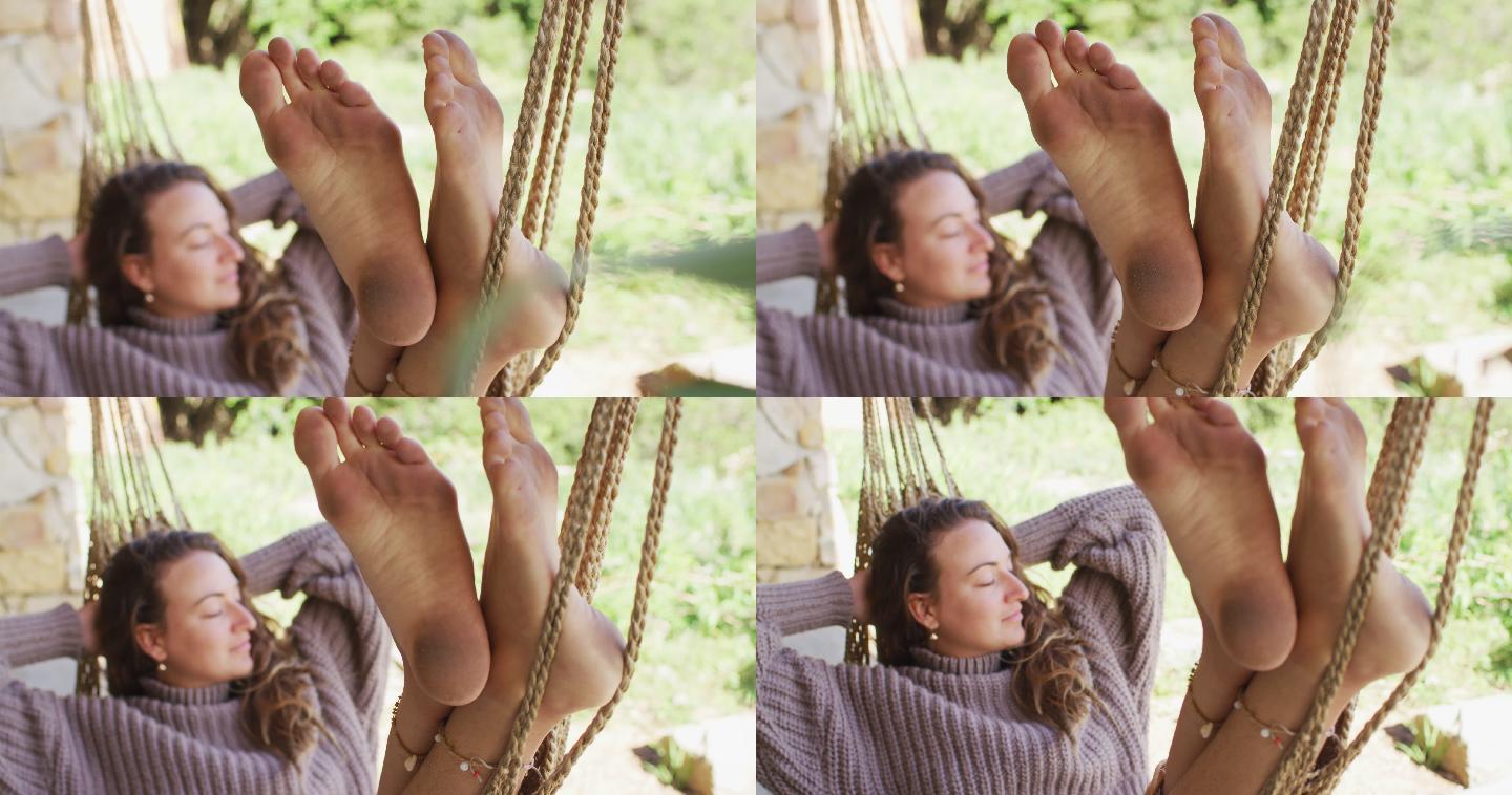微笑的白人妇女光着脚躺在吊床上，放松与眼睛闭在阳光花园