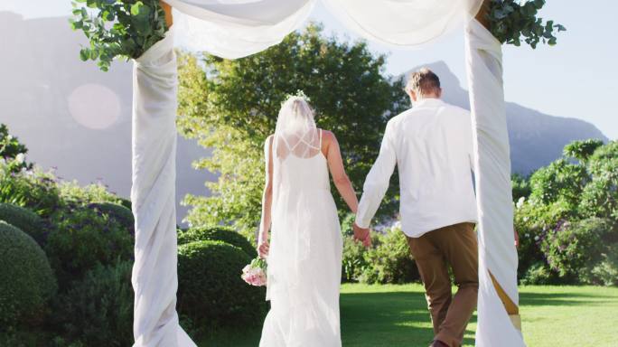幸福的白人新婚夫妇，手牵着手从室外圣坛走出来