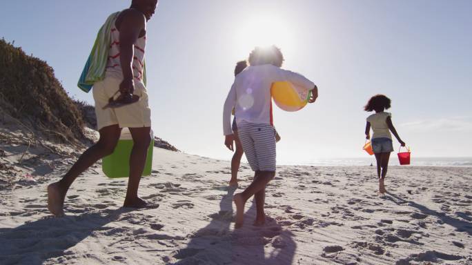 非洲裔美国人的父母和他们的孩子在海滩上带着海滩设备散步