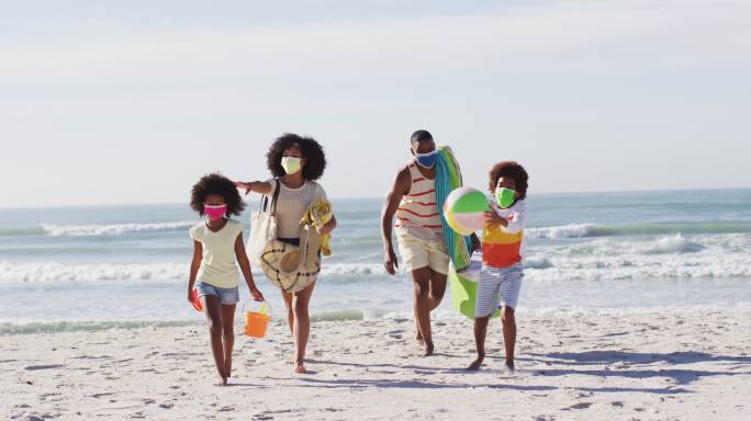 非裔美国父母和他们的孩子戴着口罩，带着海滩设备在海滩上