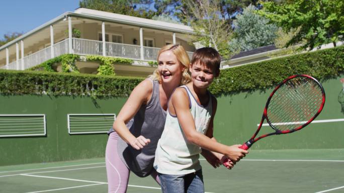 一个白人母亲在一个阳光明媚的日子在网球场教她的儿子打网球