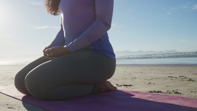 一个混血儿女人在沙滩上的瑜伽垫上冥想