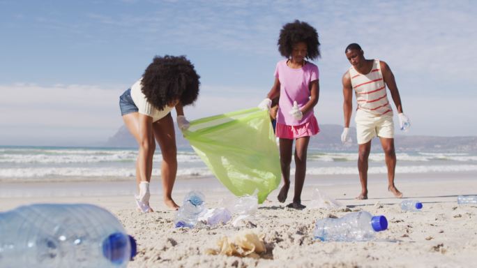 非裔美国父母和他们的孩子在海滩上捡拾垃圾和瓶子