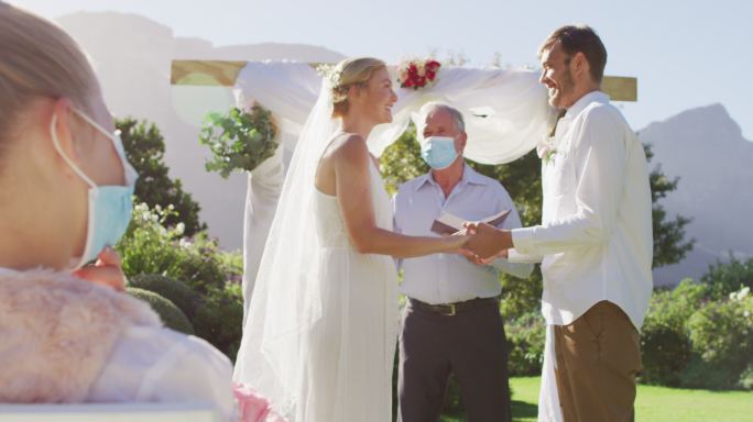 白人新娘、新郎和婚礼司仪戴着面具站在室外圣坛前
