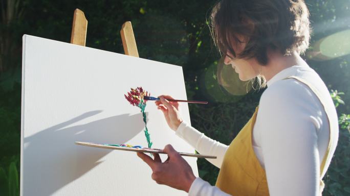 一个棕色头发的白人女人在阳光花园画画