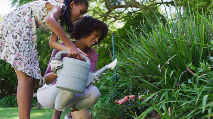 快乐的非裔美国母亲和女儿，在户外照顾植物